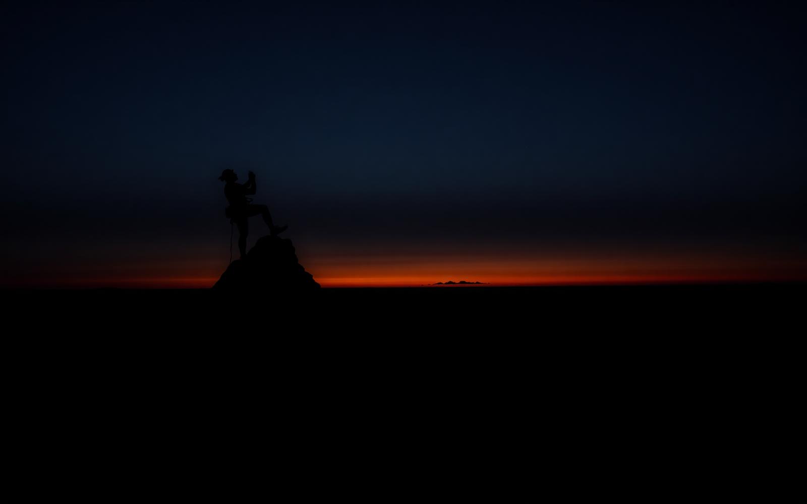 Silhouette of a climber against a deep amber horizon